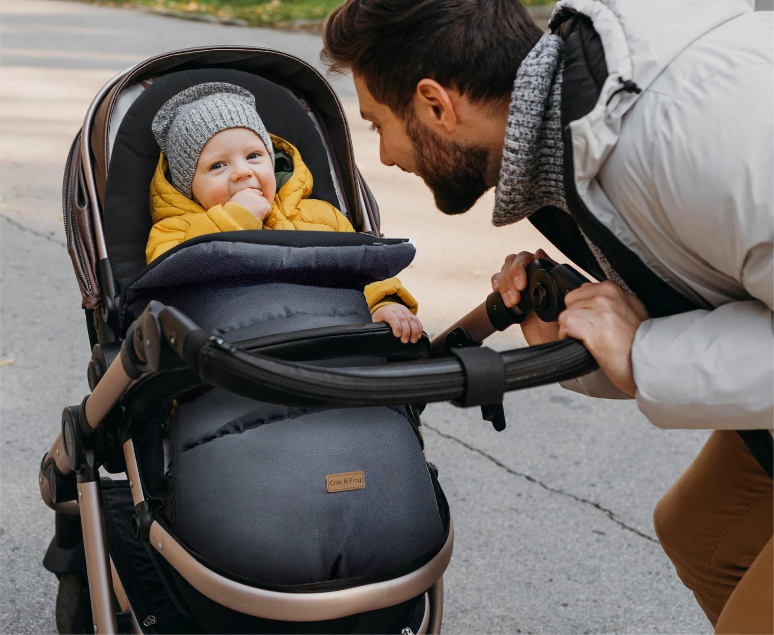 A father tucking his baby into a Croc N Frog footmuff on a winter walk
